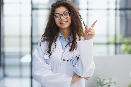 Portrait of an attractive young female doctor in a white coat points her finger