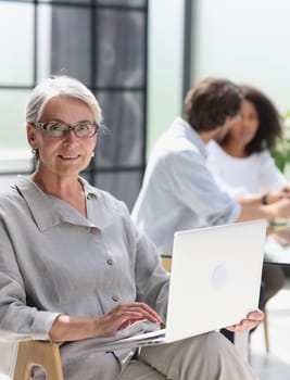 mature woman sitting with laptop looking at camera.