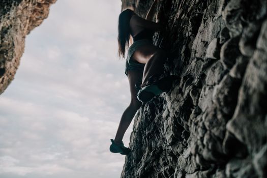 A girl climbs a rock. The athlete trains in nature. Woman overcomes difficult climbing route. Extreme hobby. Tourist woman rock climber hiking on mountains rocks over beautiful sea coast