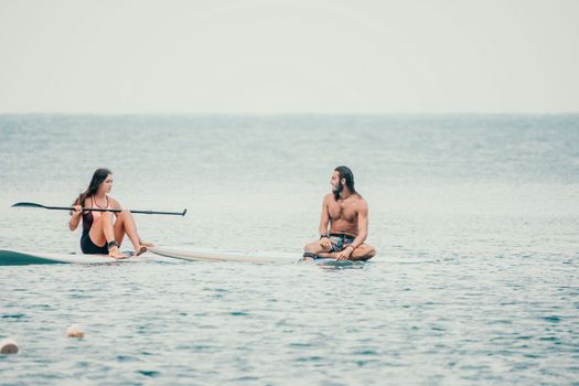 Sea woman and man on sup. Silhouette of happy young woman and man, surfing on SUP board, confident paddling through water surface. Idyllic sunset. Active lifestyle at sea or river
