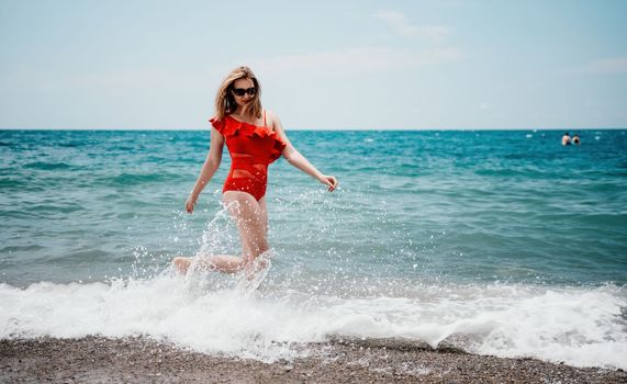 Young happy woman walks carefree on the seaside. Happy lady in red bikini. Portrait beautiful young woman relax smile around beach sea ocean in holiday vacation travel trip.