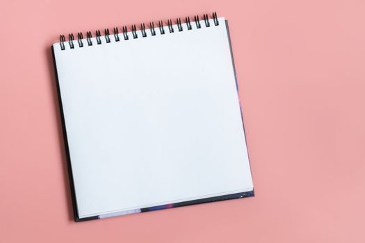 Mock up of empty spiral sketchbook with white paper on pastel pink background. Top view of open notebook with clean sheet. Template for message. Copy space