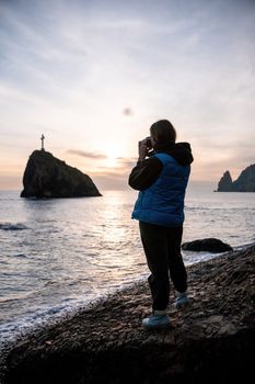 Woman travel sea. Happy tourist taking picture outdoors for memories. Woman traveler looks at the edge of the cliff on the sea bay of mountains, sharing travel adventure journey.