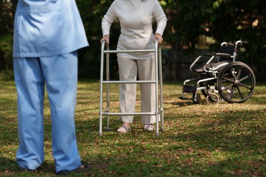 Elderly asian senior woman practice walking with aluminum walker for safety.with nurse. Nursing home hospital garden concept.