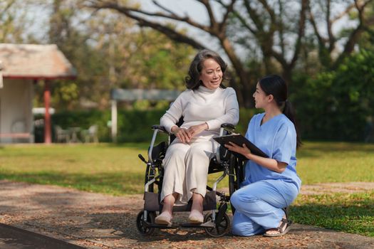 Elderly asian senior woman on wheelchair with nurse. Nursing home hospital garden concept.