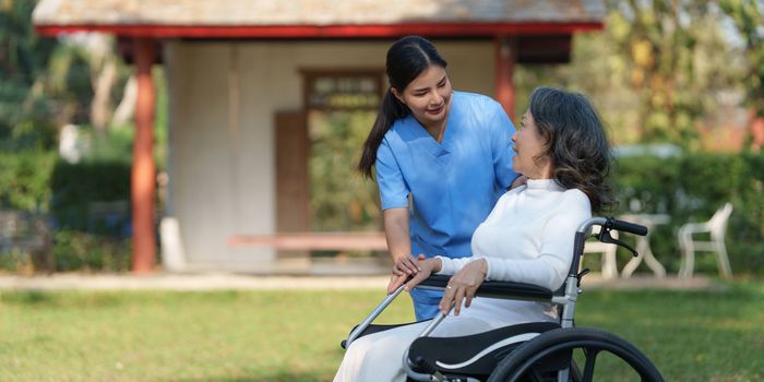 Elderly asian senior woman on wheelchair with nurse. Nursing home hospital garden concept.