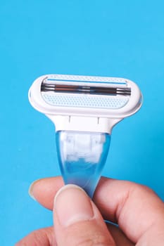 Womens blue razor in hand on a blue background close up