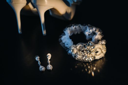 white wedding shoes and garter belt with earrings on a black background.