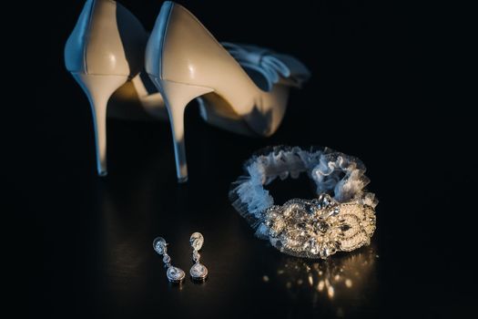 white wedding shoes and garter belt with earrings on a black background.