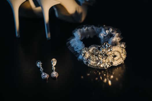 white wedding shoes and garter belt with earrings on a black background.