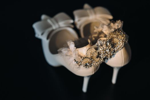 white wedding shoes and garter belt on black background.