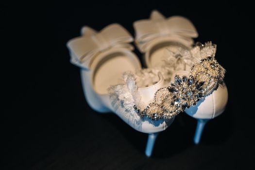 white wedding shoes and garter belt on black background.