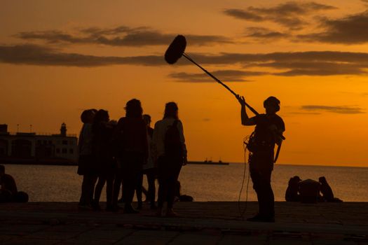 TRIESTE, ITALY - APRIL, 17: Behind the scene. Sound recorder with microphone, boom mic and headphones together the film crew team filming movie scene on outdoor location at sunset on April 17, 2018