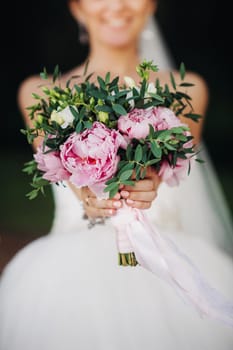 wedding bouquet with peonies in the hands of the bride under the veil.Morning of the bride.