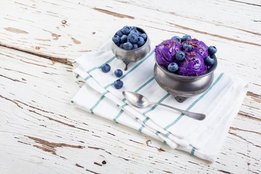 Fresh blueberry ice cream inside a pewter cup on old white wooden table