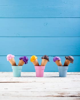 Various ice-cream scoops on blue background with assorted balls of blueberry, chocolate, strawberry and orange icecream in waffles