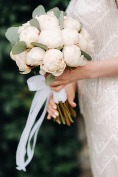 wedding bouquet with peonies in the hands of the bride at the wedding.