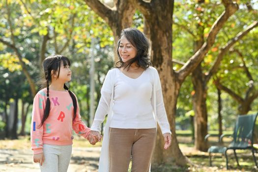 Smiling middle age grandmother and cute granddaughter walking in public park at morning.