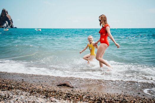 Happy loving family mother and daughter having fun together on the beach. Mum playing with her kid in holiday vacation next to the ocean - Family lifestyle and love concept.