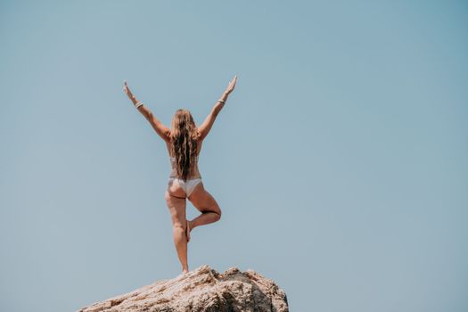 Woman meditating in yoga pose silhouette at the ocean, beach and rock mountains. Motivation and inspirational fit and exercising. Healthy lifestyle outdoors in nature, fitness concept.