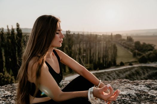 Well looking middle aged woman with long hair, fitness instructor in leggings and tops doing stretching and pilates on the rock near forest. Female fitness yoga routine concept. Healthy lifestyle.