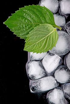 Ice cube with mint leaves on black background