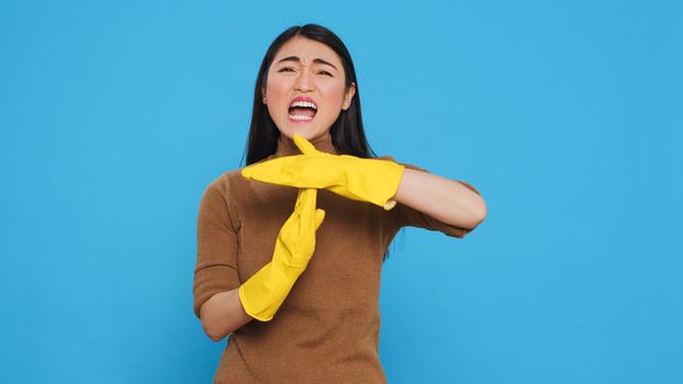 Asian homemaker doing time out gesture during house cleaning in studio over blue background. Tired housewife needed pause from work, used only the best cleaning products and equipment