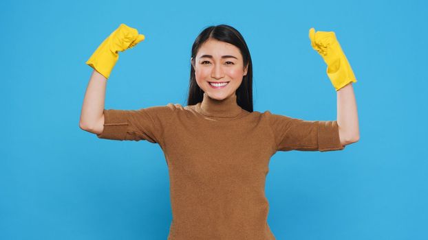 Overjoyed housekeeper wearing protective gloves while doing win gesture in front of camera after finishing housecleaning. Happy maid is a woman who is responsible for providing cleaning services