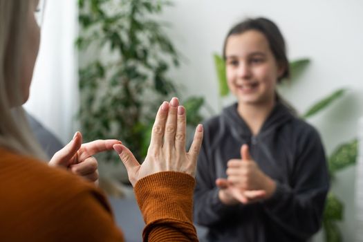 Small Caucasian teen girl child do articulation exercises with caring mother or teacher at home. Little kid pronounce sounds speak talk with tutor or coach, engaged in voice pronunciation together.