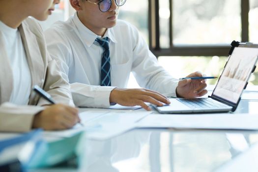 Close up businesspeople or colleagues are working together on investment project, discussing, sharing ideas, planning, and analyzing the business strategy and finance using laptop and graphs at workplace.