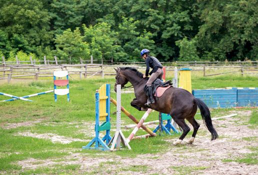 Young rider on horse jumping over obstacle on her course in competition