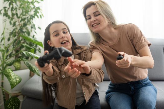 good relationship cute little girl with young mother using joystick playing video game sitting together in living room wooden floor enjoying family holiday.