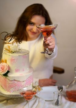 Beautiful girl raises a glass of wine. Festive cake decorated with flowers.