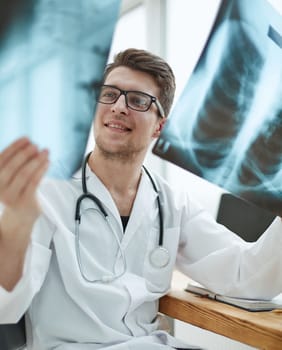 Male doctor in glass radiologist examines x-rays in a medical office.