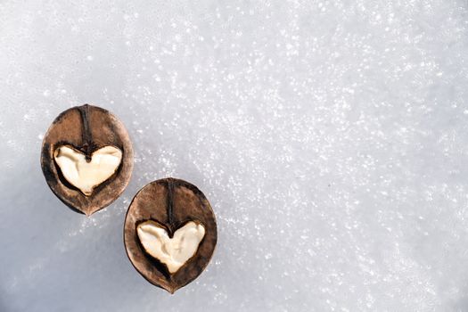 Two white hearts made of walnut halves against background of white snow, concept of love and health, copy space