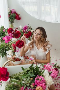 A beautiful girl in a white nightgown at home surrounded by spring flowers. A room decorated with bouquets of peonies