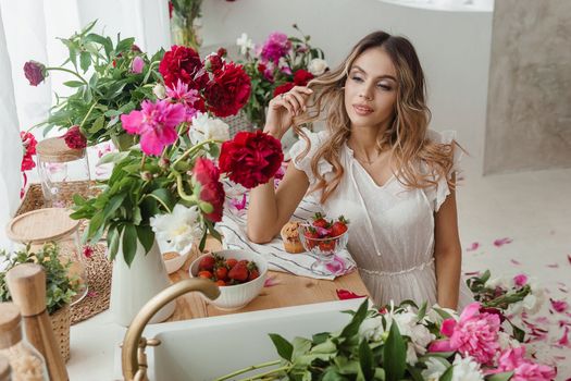 A beautiful girl in a white nightgown at home surrounded by spring flowers. A room decorated with bouquets of peonies