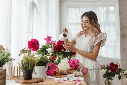 A beautiful girl in a white nightgown at home surrounded by spring flowers. A room decorated with bouquets of peonies