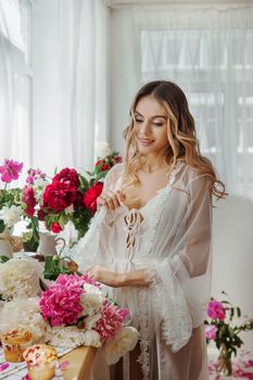 A beautiful girl in a white nightgown at home surrounded by spring flowers. A room decorated with bouquets of peonies