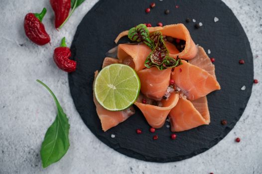 Fresh smoked salmon slices with peppers, greens and lime on concrete background