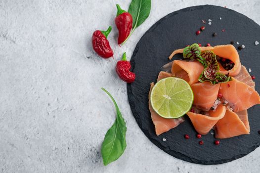 Fresh smoked salmon slices with peppers, greens and lime on concrete background
