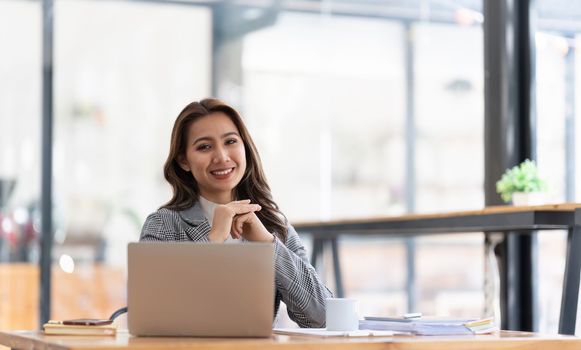 Young businesswoman working at her laptop and going over paperwork while sitting at a desk in an office.