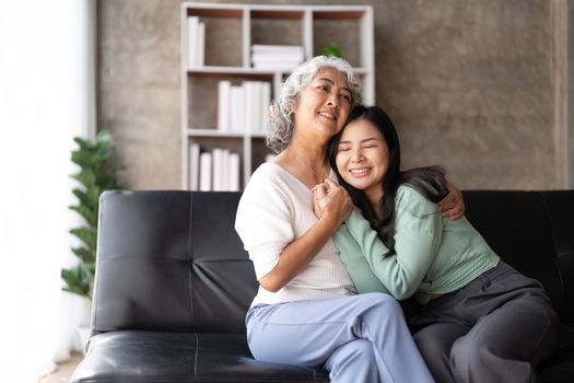 Happy daughter and mother having fun in living room, smiling mother hugging young grown daughter bonding chatting relaxing encourage each other at home together.