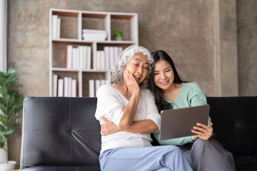 Mother up daughter sit on couch in living room hold on tablet looking at screen watching movie film, using device make video call, shopping ,daughter teach mom concept.