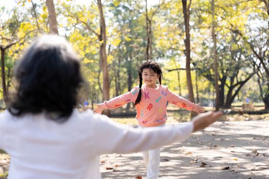An adorable granddaughter running to her grandmother, playing fun game in the park together.