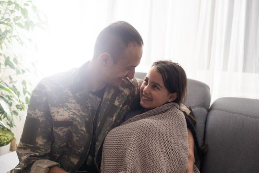 Affectionate military father kissing his daughter who is sleeping on the sofa at home.