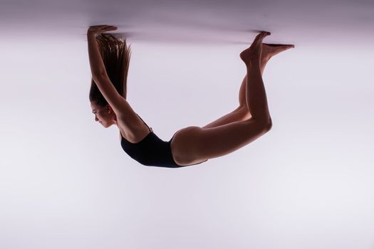 Young slim female in black bodysuit makes yoga stretching exercise on white studio background.