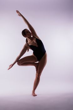 Young slim female in black bodysuit makes yoga stretching exercise on white studio background.