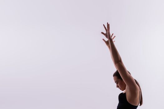 Young slim female in black bodysuit makes yoga stretching exercise on white studio background.