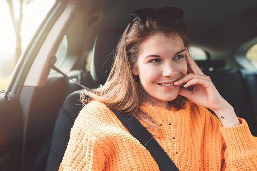 Beautiful young happy smiling caucasian woman driving in her car, wearing sunglasses and an orange sweater. High quality photo